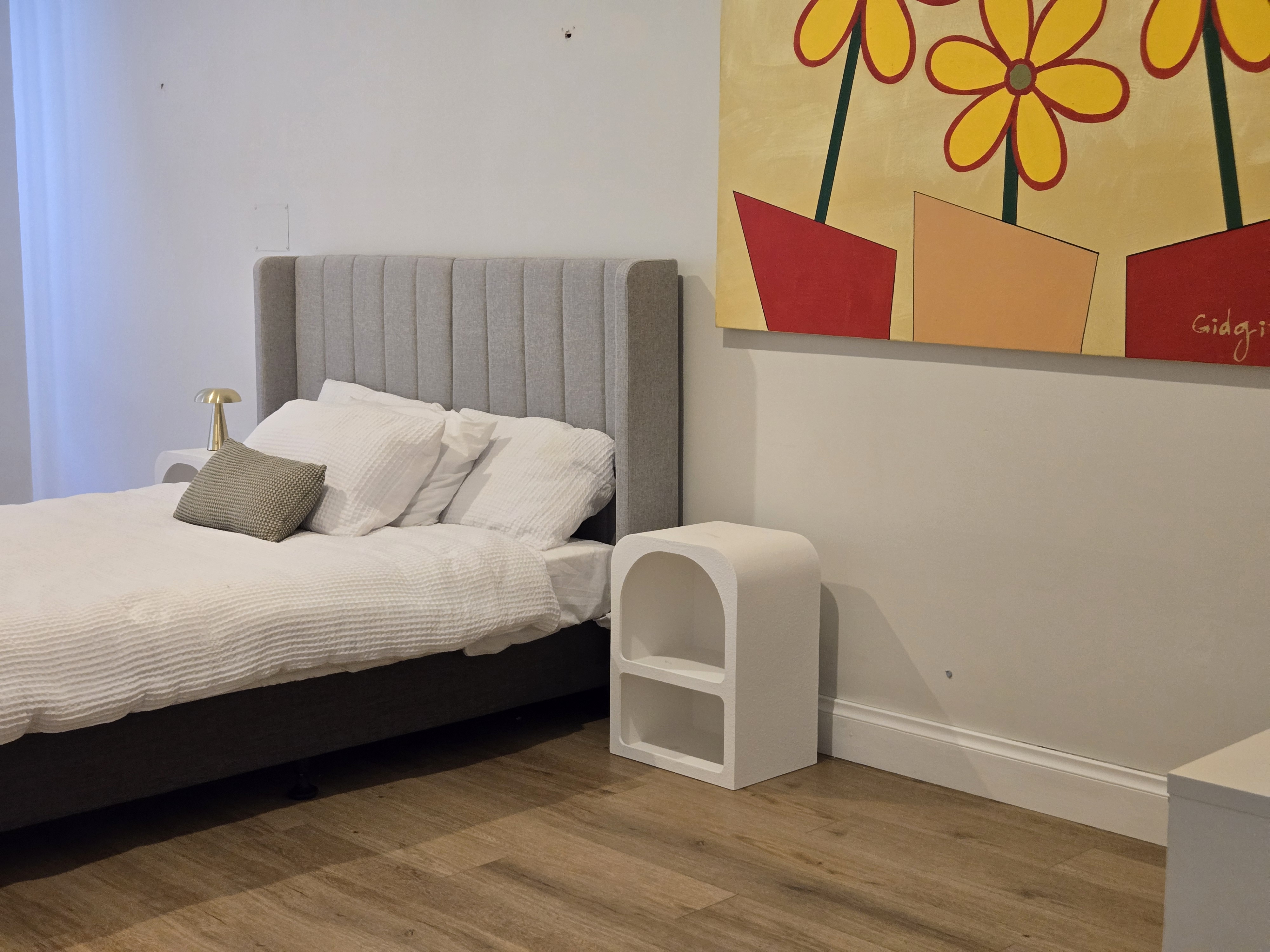 Calm private bedroom with warm timber flooring and colourful artwork at Ryrie Street