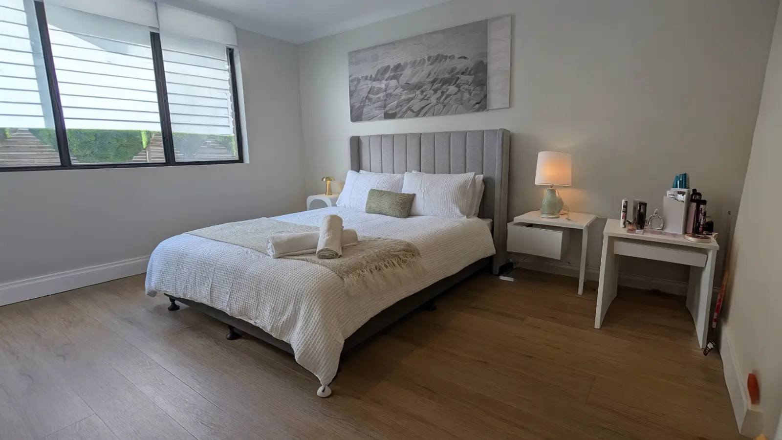 Furnished bedroom at the Ryrie Street residence with a queen bed, upholstered bedhead, bedside tables, lamp and a large window to the garden