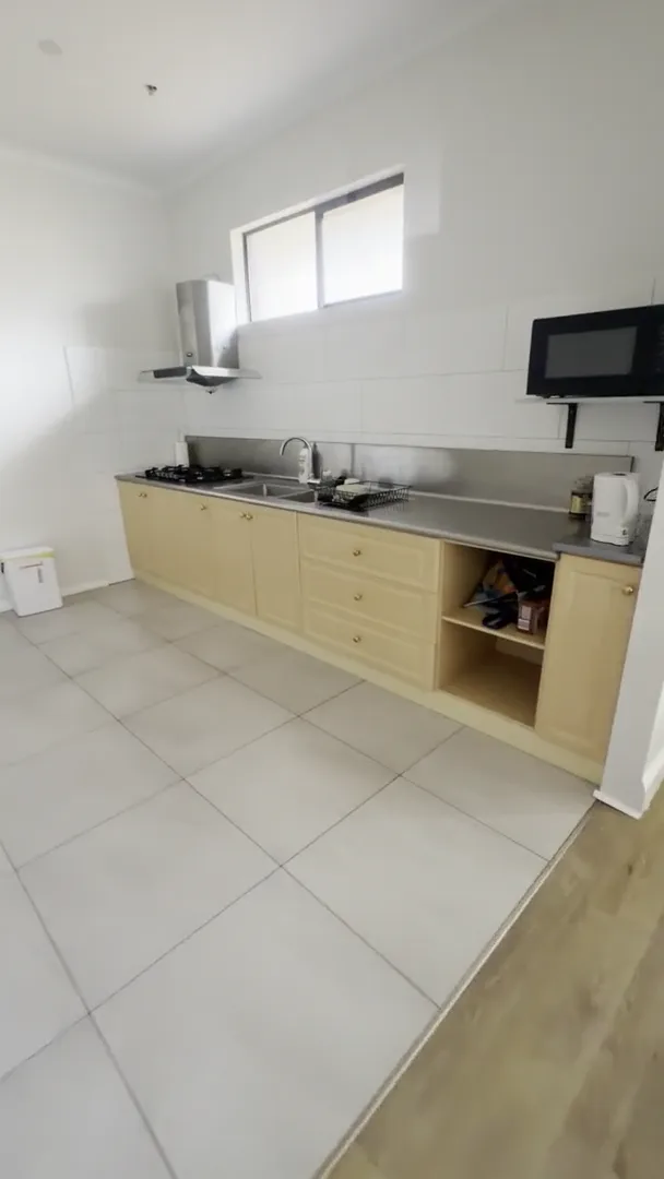 Section kitchen at the Ryrie Street residence with light timber cabinetry, a long bench, gas cooktop and microwave
