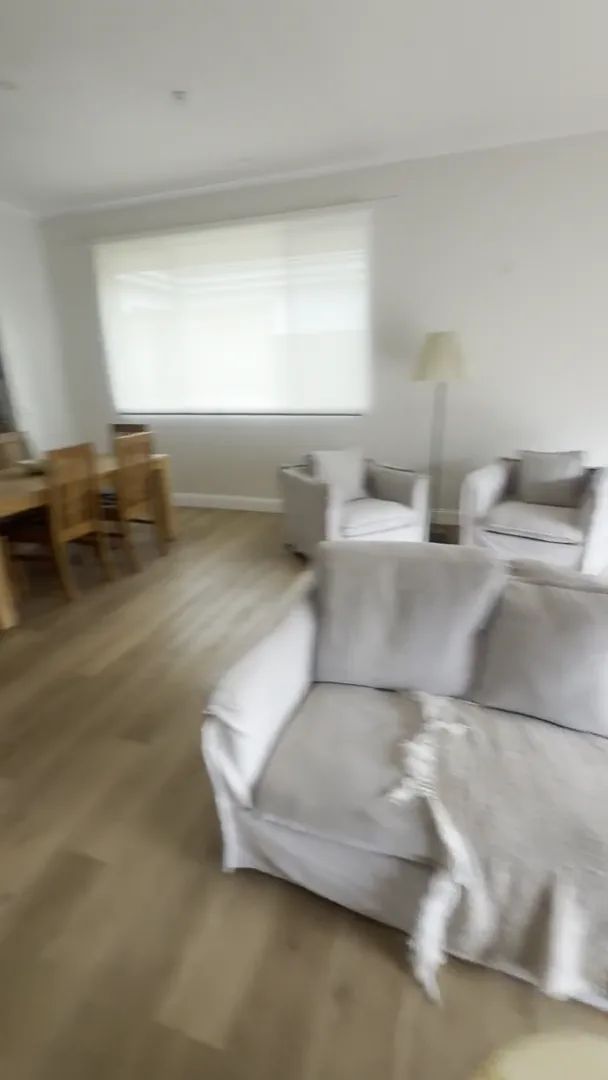 Living and dining area at the Ryrie Street residence with armchairs, a sofa, timber flooring and a dining table beside the window